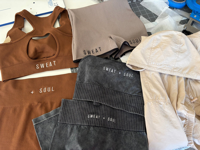 Collection of 'SWEAT + SOUL' branded clothing items on a table.